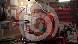 Old man repairing a bicycle in garage, bicycle mechanic unscrewing the seat with screwdriver in workshop interior