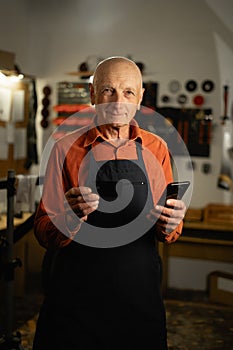 Old man repairing his bicycle standing holding credit card and mobile phone smiling at the camera.