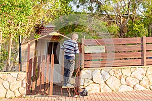 Old Man Repairing Wooden Gate Near Home.