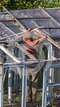 The old man repairs the greenhouse in the garden