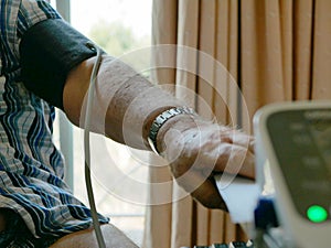 An old man`s arm with a pressure cuff on checking his blood pressure at home by himself