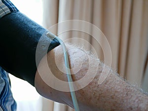 An old man`s arm with a pressure cuff on checking his blood pressure at home by himself