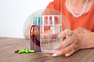 The old man`s hand holding a glass of water is preparing to take medicine