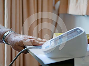 An old man`s hand placed next to the monitor checking his blood pressure at home by himself