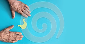 old man's hands and stomach symbol cut out of yellow paper on a blue background, banner, copyspace . stomach