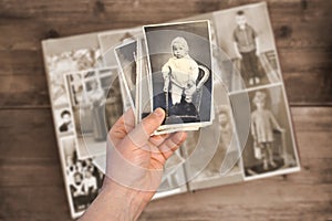 Old manÃ¢â¬â¢s male hands hold old retro family photos over an album with vintage monochrome photographs in sepia color, the concept photo