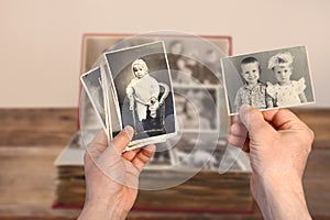 Old manÃ¢â¬â¢s male hands hold old retro family photos over an album with vintage monochrome photographs in sepia color, genealogy