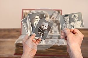 Old manÃ¢â¬â¢s male hands hold old retro family photos over an album with vintage monochrome photographs in sepia color and wooden photo