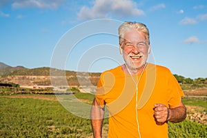 Old man or senior running alone in a rural zone around the nature and houses - one mature male doing exercise and losing weight