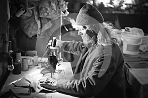 Old man sewing cloth bw