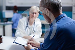 Old man signing appointment papers for healthcare system at checkup visit