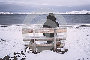 old man sits alone on a bench against the backdrop of the bay. concept of loneliness and solitude. Cold winter landscape. A man