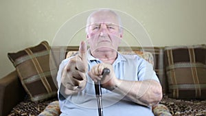 Old man sitting in a chair and holding a cane in his hands shows gesture ok
