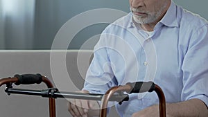 Old man sitting and looking at walking frame, spine trauma, indecisiveness