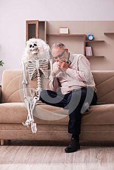 Old man sitting on the sofa with the female skeleton