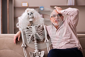 Old man sitting on the sofa with the female skeleton