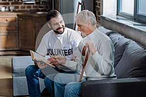 Old man sitting with a volunteer and looking at his favorite book