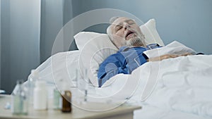 Old man sleeping in bed at hospital ward, antibiotics standing on the table photo