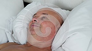 Old man sleeping in bed on white bedding, concept of business trip, travel, sound healthy sleep, problem of insomnia, noise