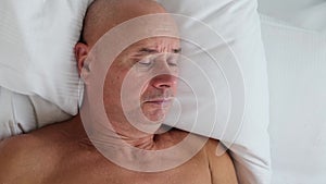 Old man sleeping in bed on white bedding, concept of business trip, travel, sound healthy sleep, problem of insomnia, noise