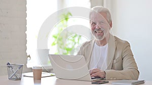 Old Man Smiling at Camera while using Laptop in Office