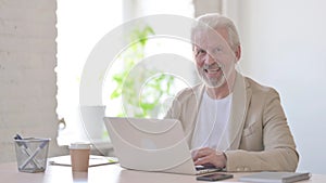 Old Man Smiling at Camera while using Laptop in Office