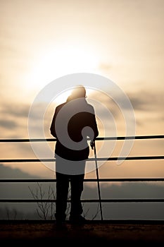 Old man standing in sunset with cane