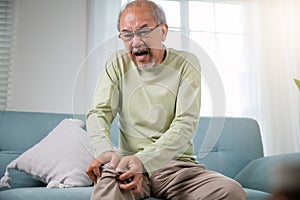 Old man suffering from knee joint pain on sofa living room