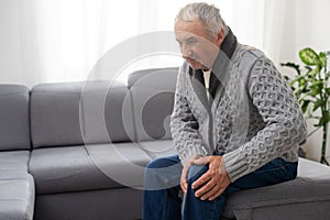 Old man suffering from knee pain sitting sofa