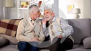 Old man talking to deaf friend sitting on sofa at home, hearing disease, problem