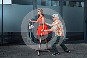 Old man teaches to ride a skateboard young girl.