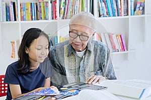 Old man teaching his granddaughter to read a book