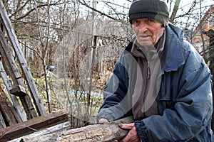 An old man in untidy clothes chooses from a pile of old wood boards to heat the house, loneliness in the village