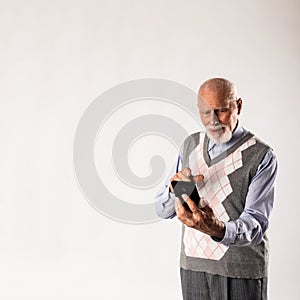 Old man is using a smart phone on gray background with copy space