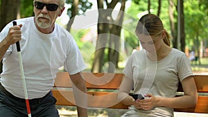 Old man with visual impairment sitting on bench near angry and displeased girl