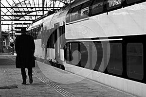 Old man walking along a train of an empty platform whom is travelling or said goodby to someone - BW