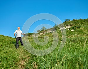 Old man walking on green field with tracking sticks.