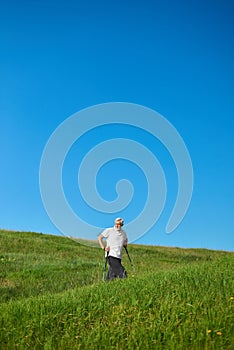 Old man walking on hills with tracking sticks.