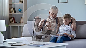 Old man watching photo album with grandson, recalling stories from happy youth