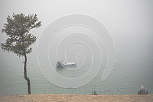 Old man wathing at lonely boat on Lake Baikal under the fog