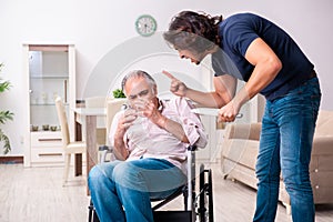 Old man in wheel-chair and young bad caregiver indoors