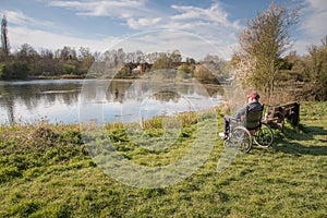 Old man in a wheelchair overlooking a calm lake on a warm afternoon,Hampshire,UK