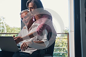 Old man who uses wheelchair laughing at something on laptop