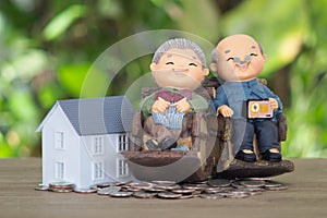 The old man and wife model are placed on a pile of dollar coins and a small house model next to it
