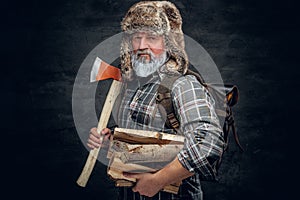 Old man woodman holding hatchet and stack of lumber