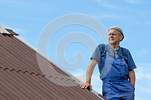 Old man working, building a roof of a house without any safety devices, wearing work clothes, blue overall, on a warm sunny day, d