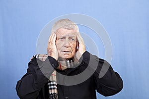 An old man with a worried expression and his hands pressed to his head