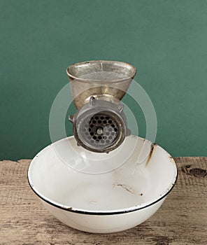 Old manual meat grinder and a white enamel bowl