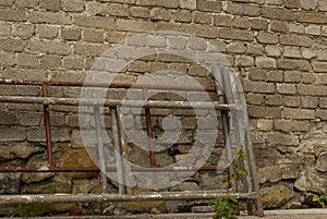 An old masonry wall made of bricks and stones and construction scaffolding lying next to it.