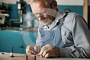 An old master with glasses works in a workshop